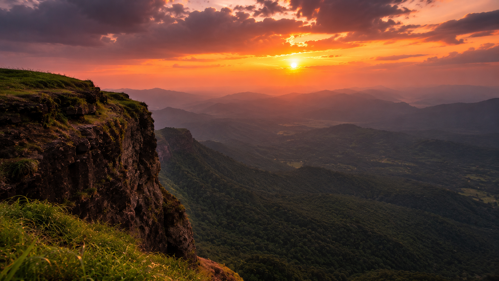 sunset over a cliff-edge viewpoint in the Western Ghats, warm orange and pink sky reflecting over layered valleys, silhouetted hill ridges in the distance