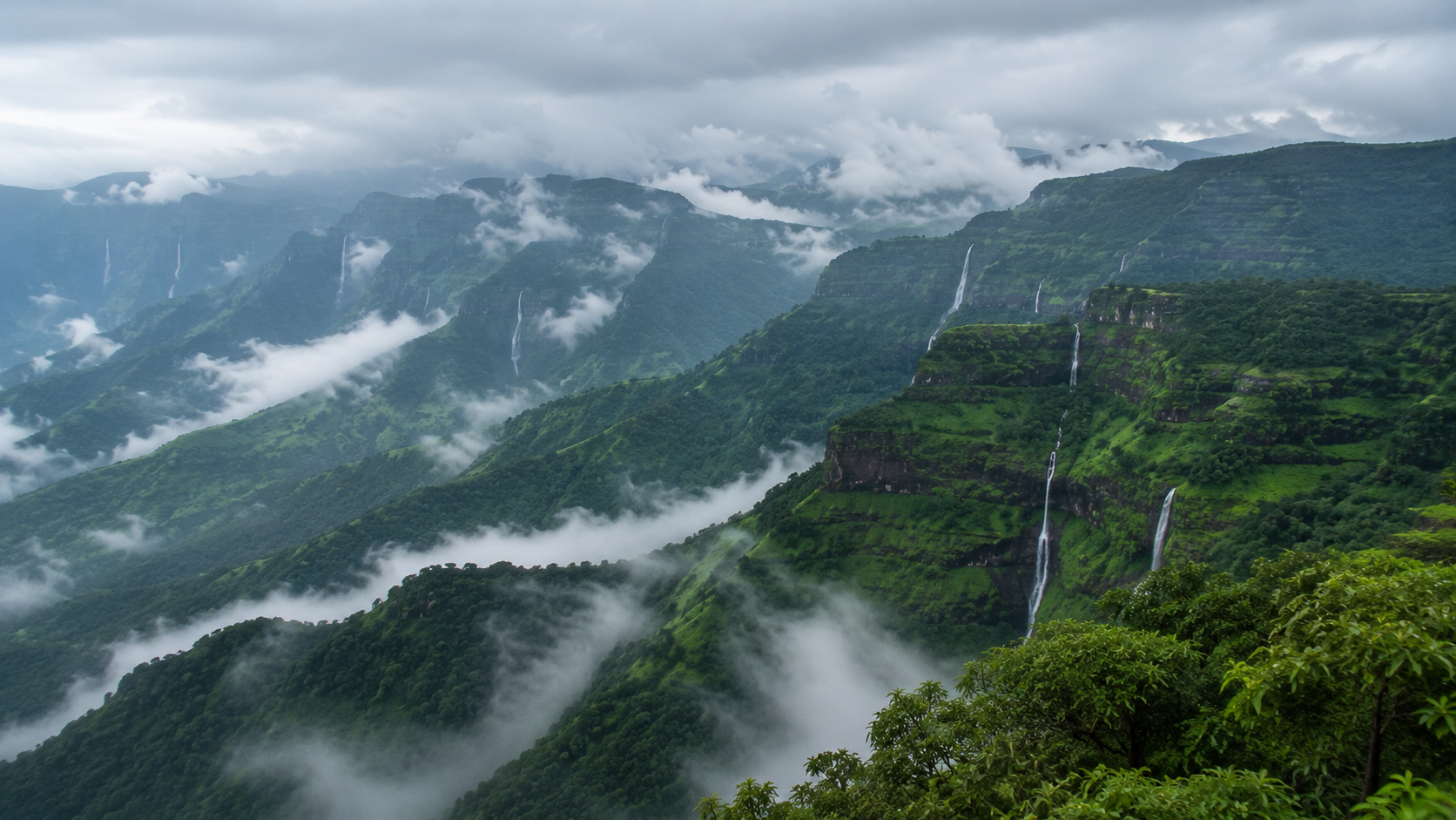 Sweeping panoramic view of layered Sahyadri hills during monsoon, deep green slopes streaked with multiple waterfalls, low clouds settling in the valleys, soft natural lighting