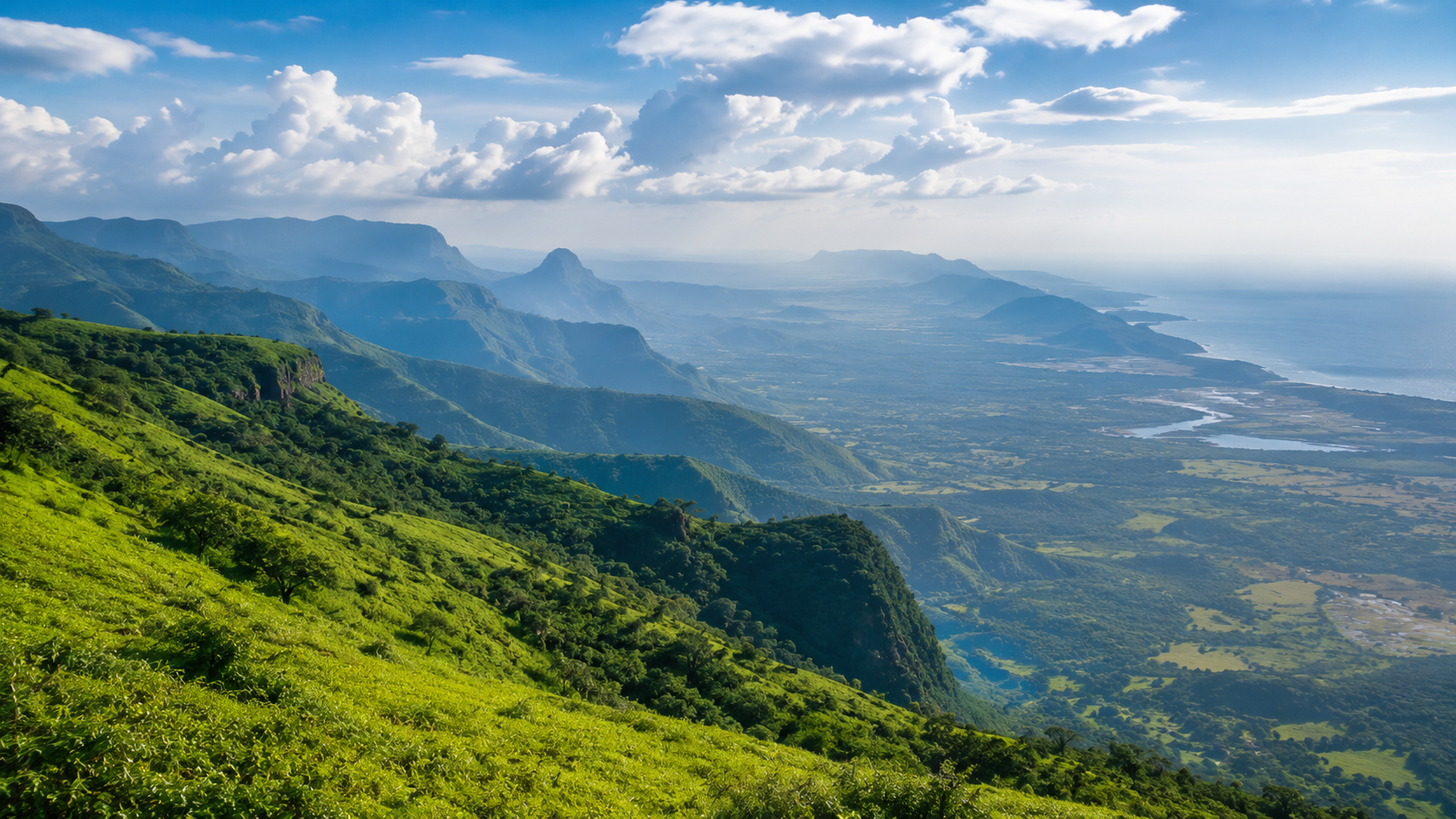Sweeping panoramic view combining layered green Sahyadri hills fading into a coastal plain and the sea in the far distance