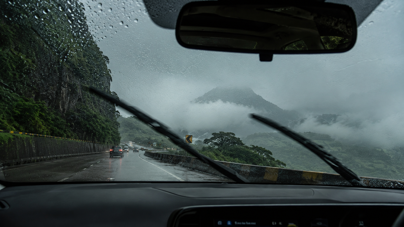 View through a car windshield of the rainy Mumbai-Pune Expressway ghat road surrounded by green hills