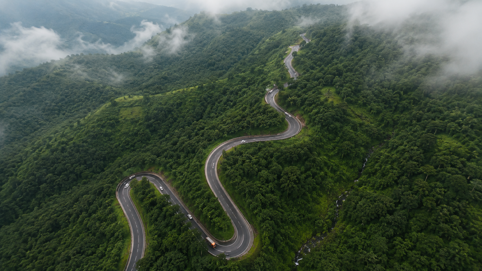 Aerial drone view of a winding ghat road cutting through green Sahyadri hills near Mahabaleshwar