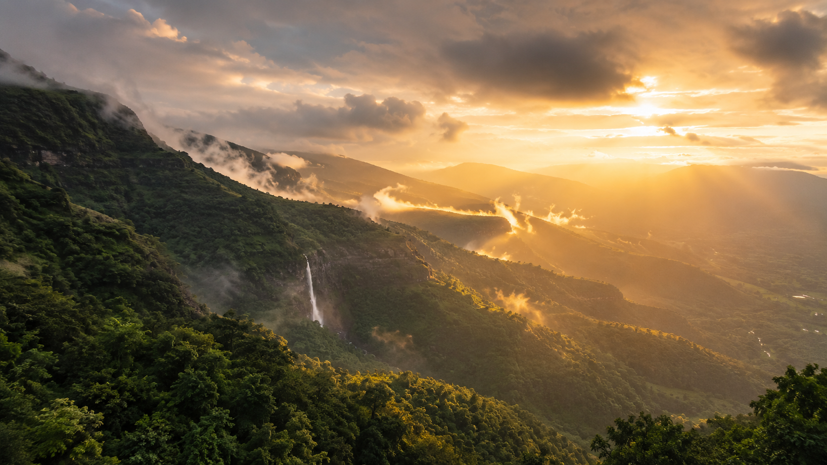 Golden sunrise light breaking through monsoon clouds over the green Malshej Ghat valley