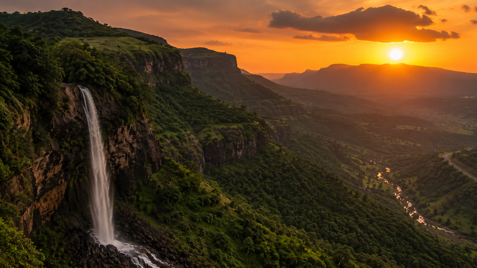 Orange sunset sky over the green Malshej Ghat valley with a waterfall visible in the foreground