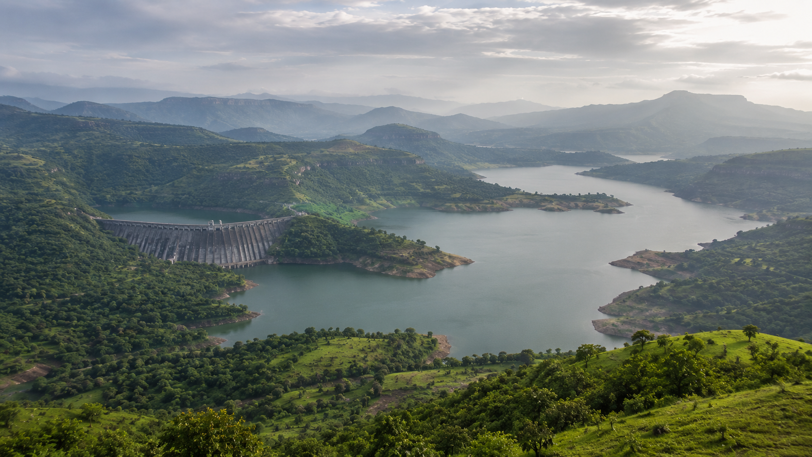 Wide panoramic view of the green Bhandardara valley with Wilson Dam and surrounding hills